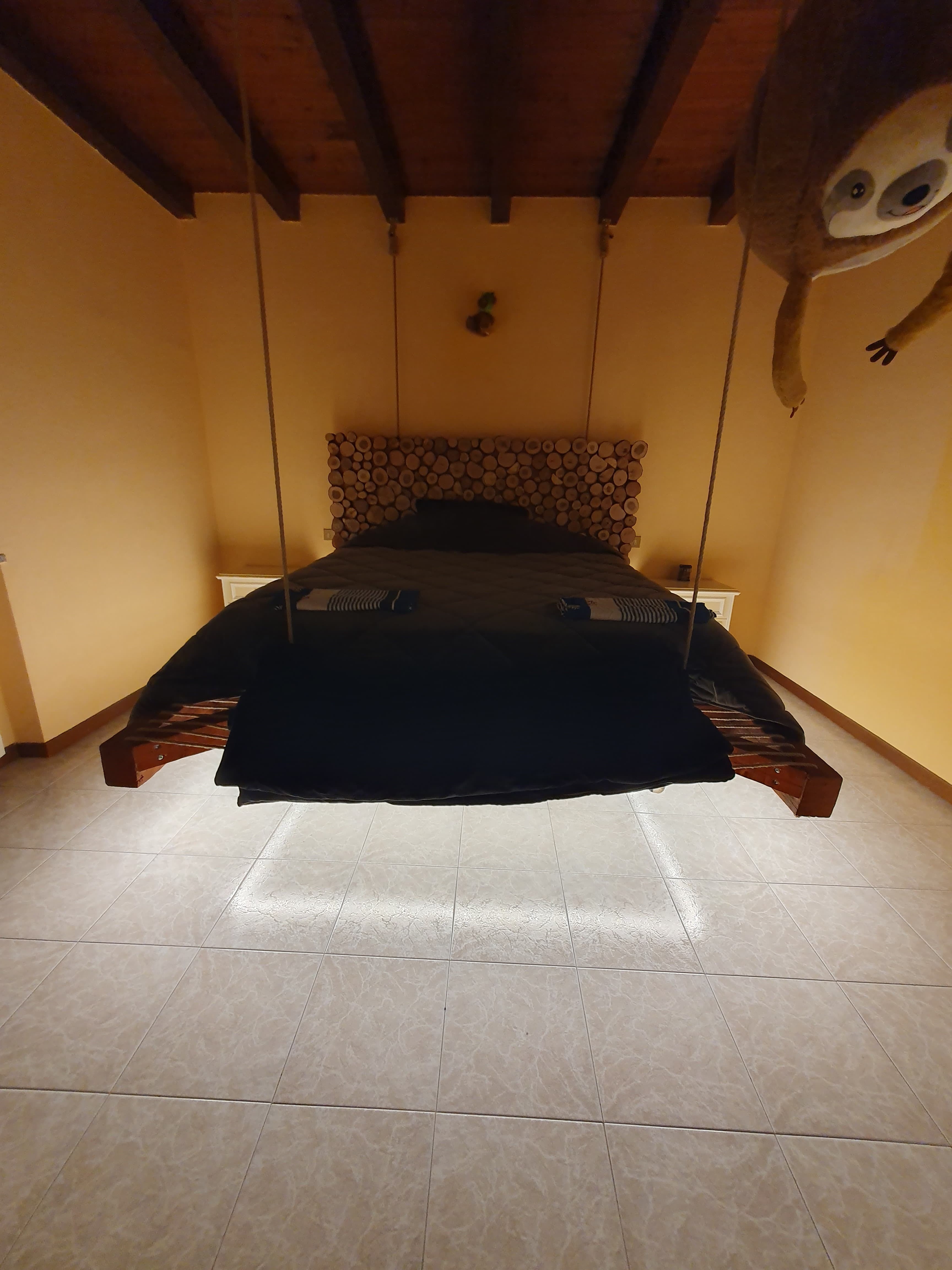 Letto matrimoniale sospeso con corde dal soffitto in legno di una mansarda